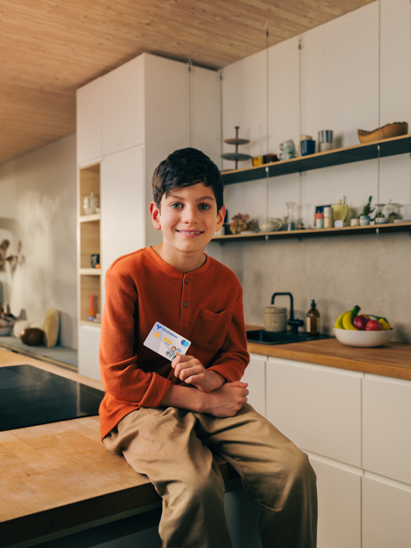Ein Bub sitzt auf einem Tisch in der Küche und hält eine Volksbank Jugend Sparkarte in der Hand.