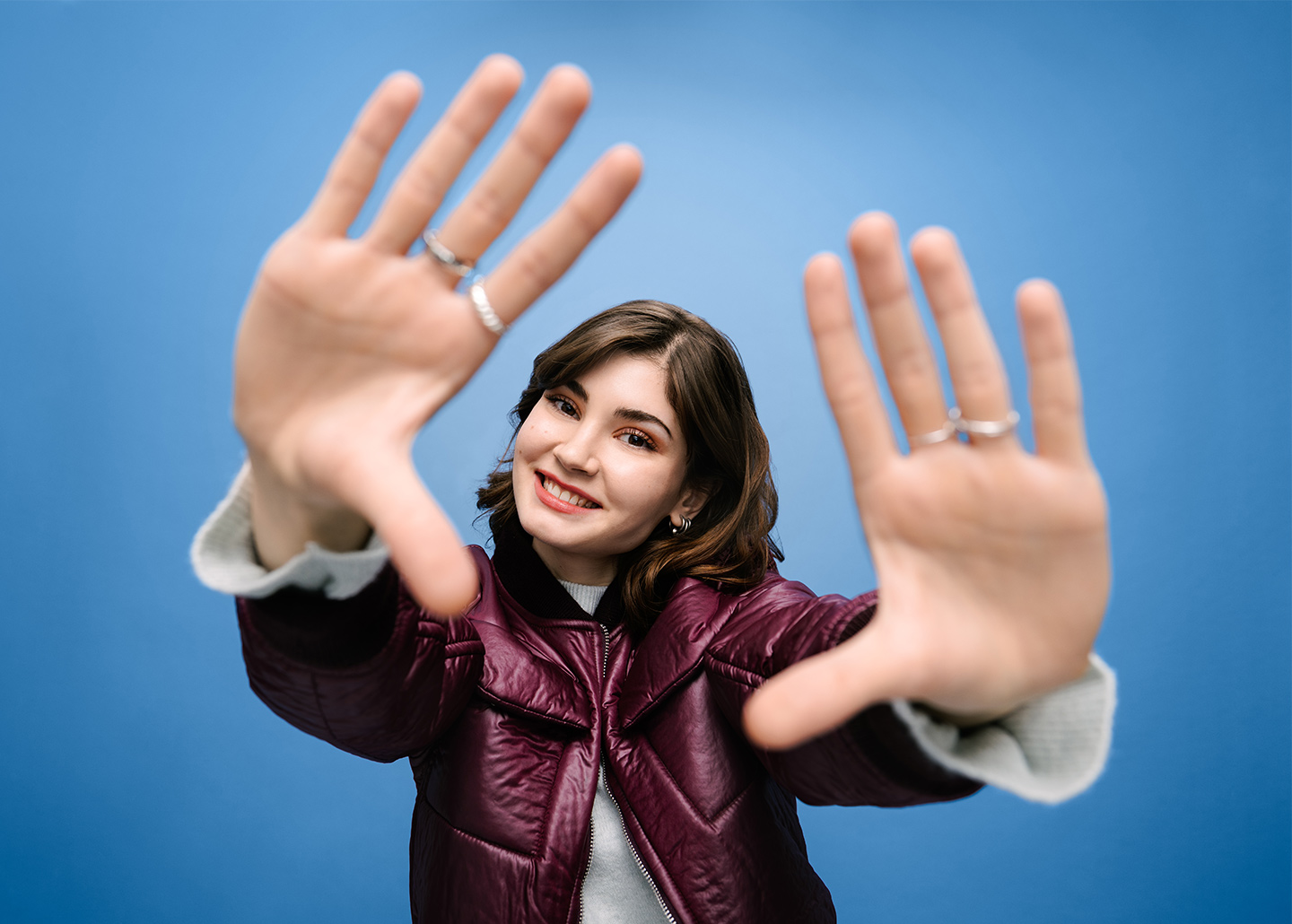 Eine junge Frau streckt ihre offenen Hände der Kamera entgegen und lächelt.